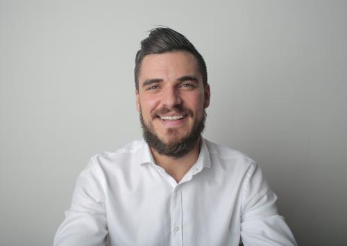 Young white man sitting in front of a white wall smiling